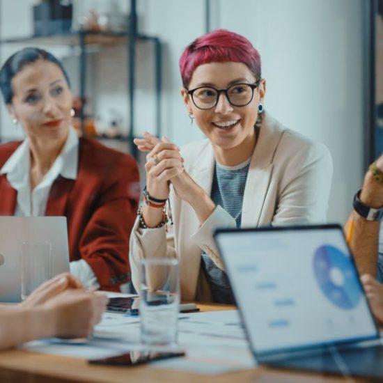 Office Meeting in Conference Room: Beautiful Specialist with Short Pink Hair Talks about Firm Strategy with Diverse Team of Professional Businesspeople. Creative Start-up Team Discusses Big Project